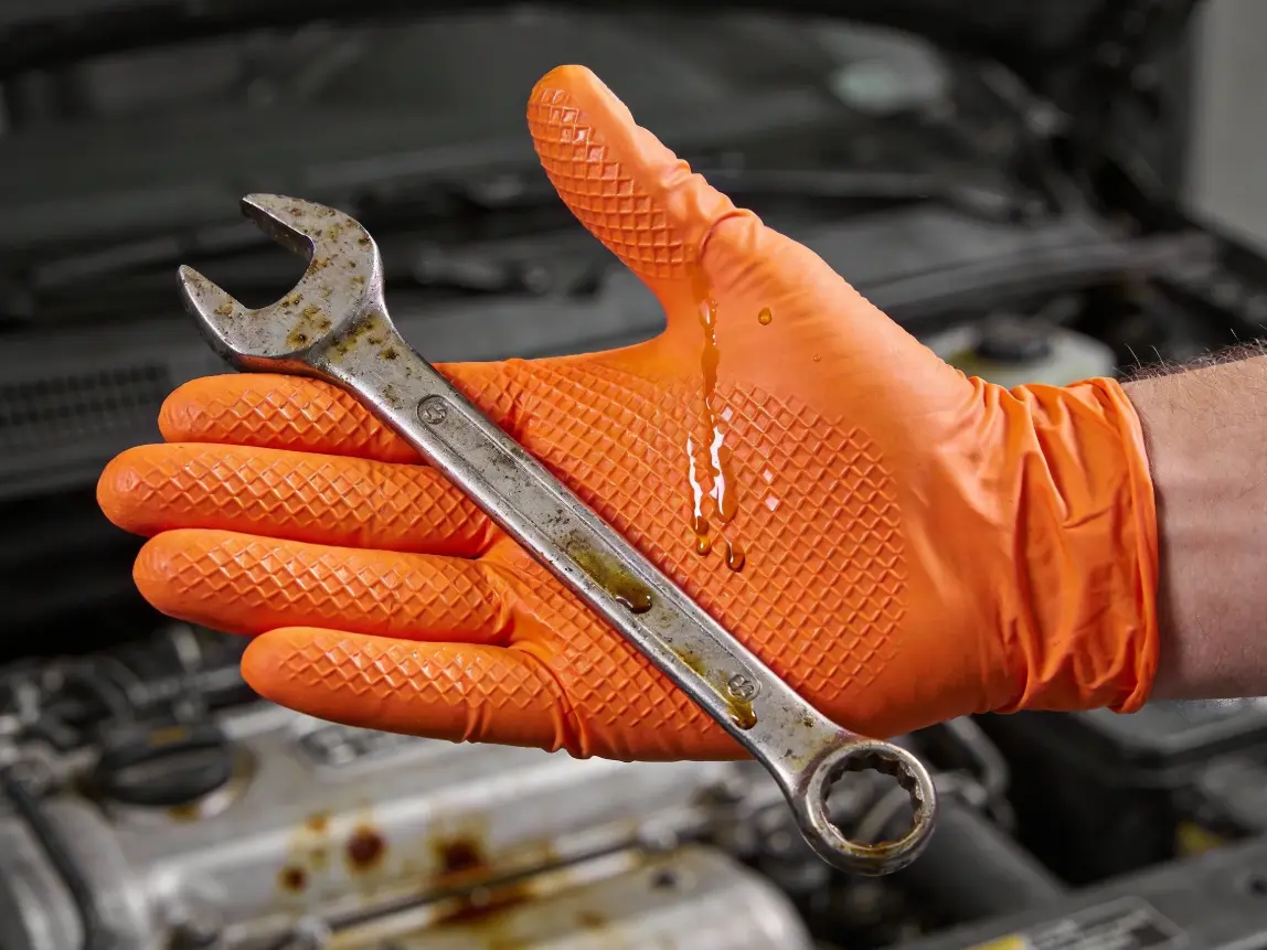 Mechanic wearing orange diamond-textured nitrile gloves gripping oily wrench in auto repair bay